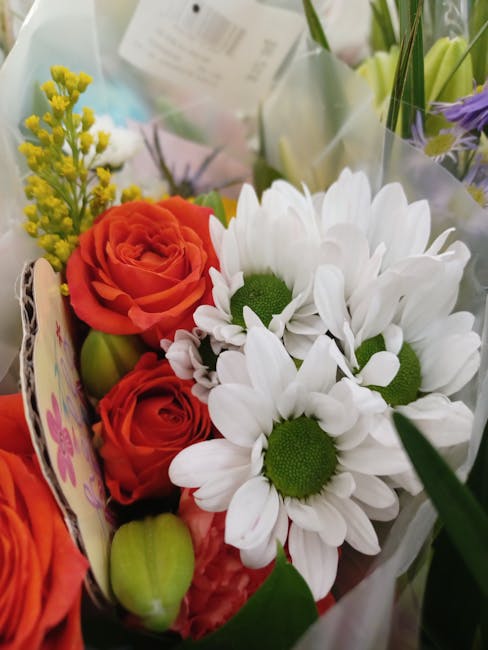 A vibrant floral arrangement featuring bright orange roses with tightly curled petals, complemented by white daisies with green centers and slightly curved petals. The bouquet also includes small clus