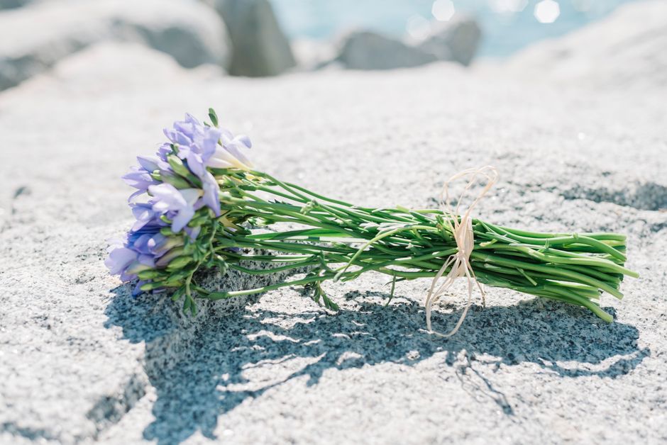 A delicate bouquet of light purple and violet flowers, featuring lisianthus and small greenery, arranged in a natural style. The flowers are tied together with a simple, beige twine, and the bouquet r